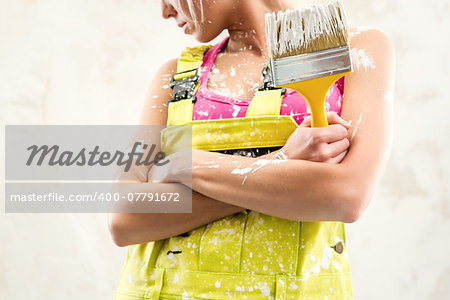 Female in coverall holding paint brush over obsolete white wall