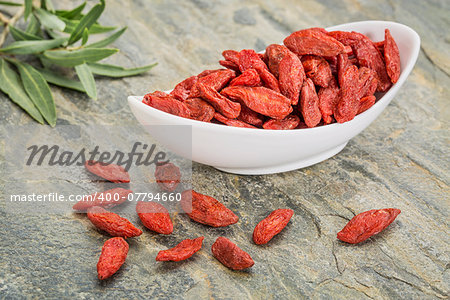 a bowl of dried Tibetan goji berries (wolfberry) with a fresh goji leaf on a slate rock  surface