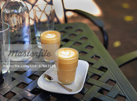 Two cortado coffees in glasses on outdoor, patio table with water bottle and glass, Canada