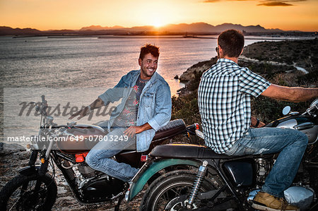 Portrait of two male motorcyclist friends on coast at sunset, Cagliari, Sardinia, Italy