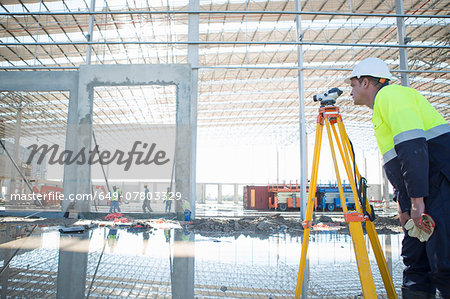 Surveyor using tripod and level on construction site
