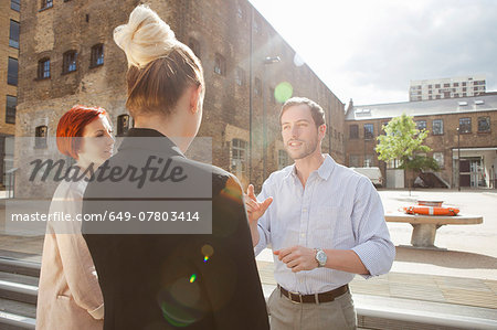 Three young people talking, building in background, East London, UK