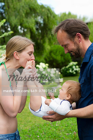 Mother kissing baby daughters feet in garden