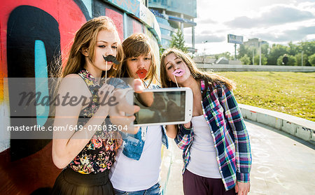 Friends taking selfie wearing fake lips and moustache, mural in background Friends taking selfie wearing fake lips and moustache, mural in background