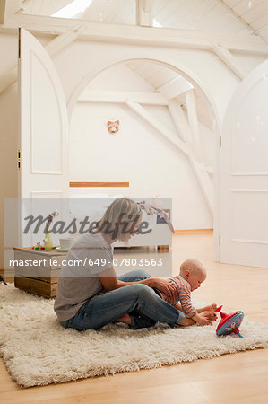 Mature mother and baby daughter playing on rug in sitting room