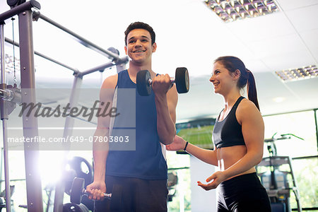 Personal trainer helping young man lift hand weights