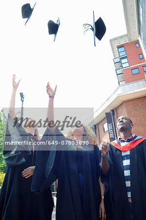 Three college students throwing graduation caps mid air