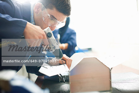 Male student using hand drill in college workshop