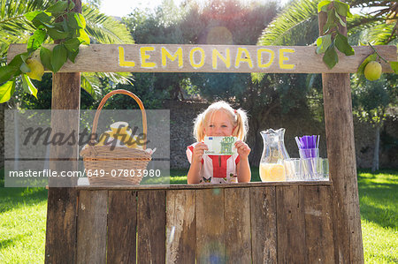 Portrait of girl on lemonade stand holding up one hundred euro note