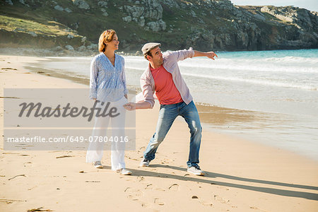 Mature couple throwing pebbles out to sea, Camaret-sur-mer, Brittany, France