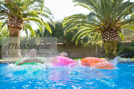 Three children splashing on inflatable rings in garden swimming pool