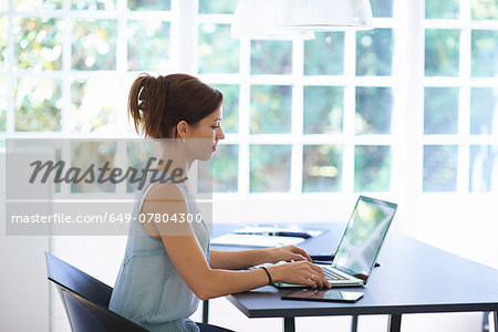 Mid adult woman working on laptop in dining room