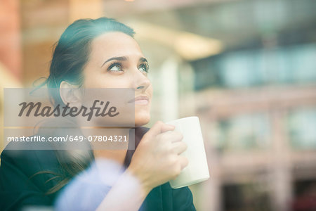 Young businesswoman drinking coffee and looking out of cafe window, London, UK