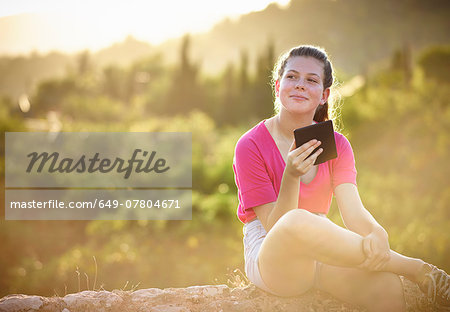 Teenage girl sitting on stone wall using digital tablet, Majorca, Spain