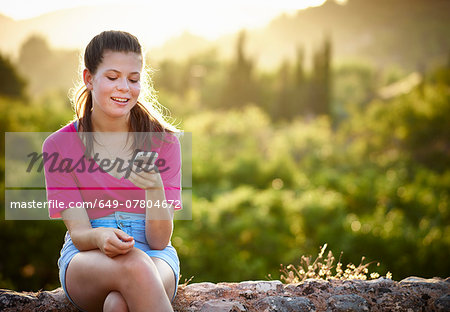Teenage girl sitting on stone wall looking at smartphone, Majorca, Spain