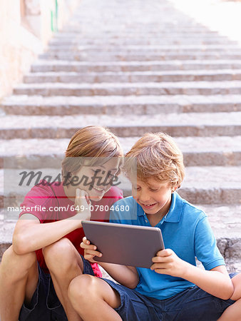 Brothers looking at digital tablet on village steps, Majorca, Spain