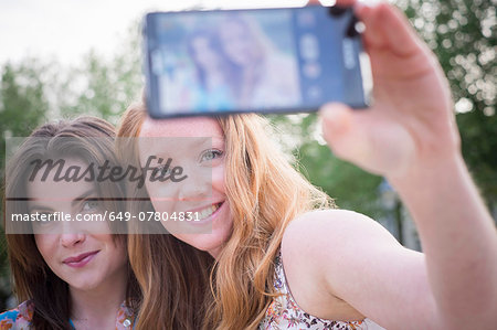 Close up of two young female friends in park taking selfie on smartphone