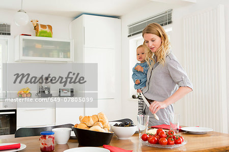 Mother setting kitchen table while holding baby daughter