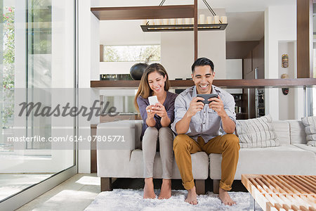 Couple playing games on smartphones on sitting room sofa