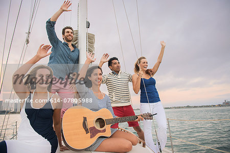 Friends on sailing boat waving, woman with guitar