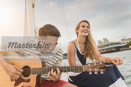 Young couple on sailing boat, man playing guitar