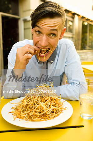 Young man eating skinny french fries at sidewalk cafe