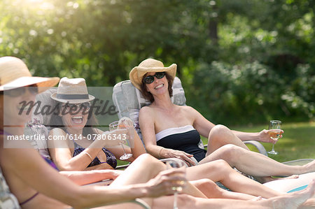 Three mature women relaxing in sun loungers, drinking wine