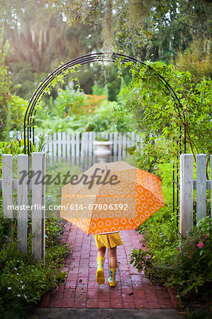 Girl walking through garden gate carrying umbrella