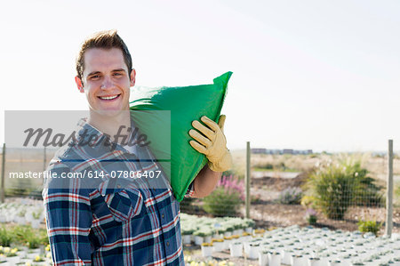 Portrait of young male worker carrying sack on shoulders at plant nursery