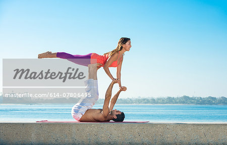 Young man and woman practicing yoga on pier at Pacific beach, San Diego, California, USA