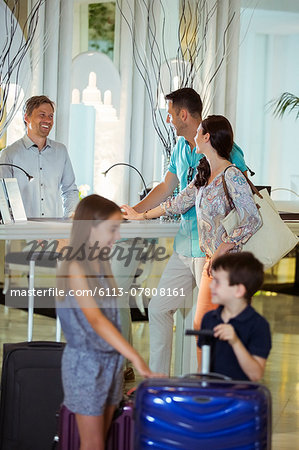 Family with suitcases talking with receptionist in hotel lobby