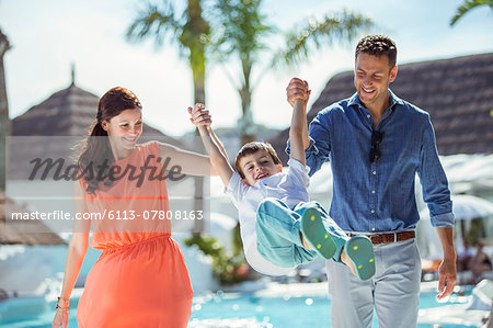 Boy holding hands with his parents by swimming pool