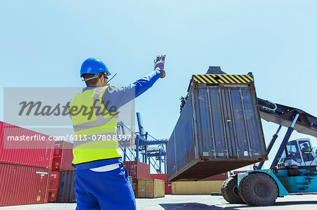 Worker directing crane carrying cargo container