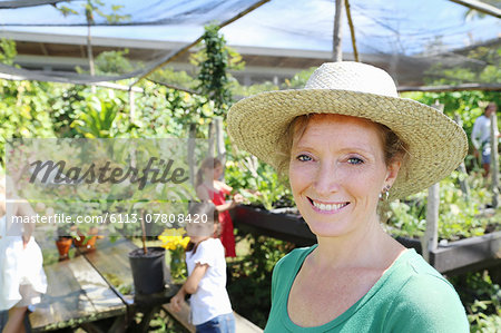 Portrait f smiling woman wearing sunhat in greenhouse, children in background