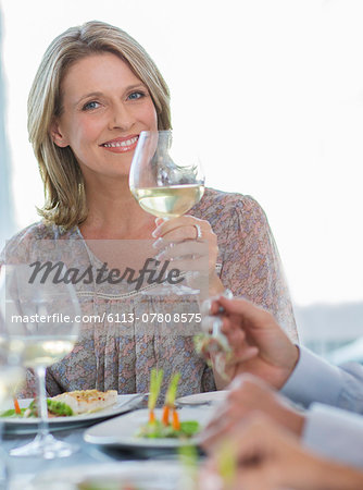 Portrait of smiling woman holding glass of white wine at restaurant table