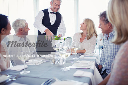 People sitting at restaurant table, waiter pouring white wine