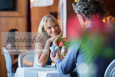 Man giving gift to smiling woman at restaurant table