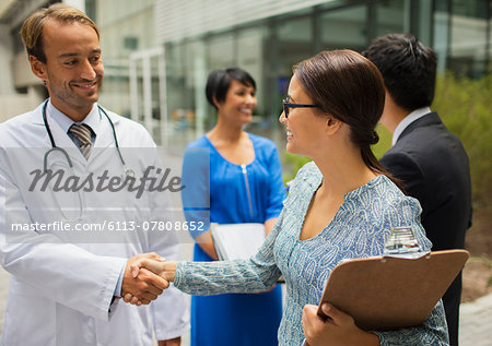 Smiling doctor shaking hand with woman in front of hospital