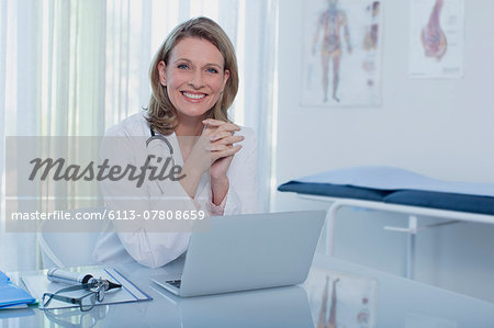 Portrait of smiling female doctor sitting at desk with laptop Portrait of smiling female doctor sitting at desk with laptop