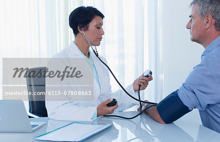 Female doctor taking patient's blood pressure in office Female doctor taking patient's blood pressure in office