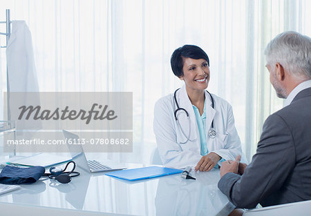 Smiling female doctor talking to patient at desk in office