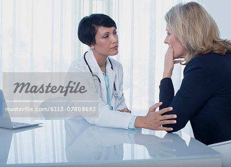 Female doctor consoling sad woman at desk in office