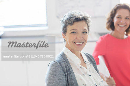 Portrait of smiling mature businesswoman with colleague in background