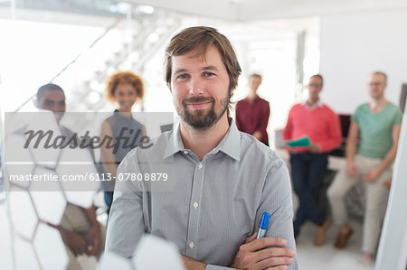 Portrait of smiling businessman wearing gray shirt, office team in background