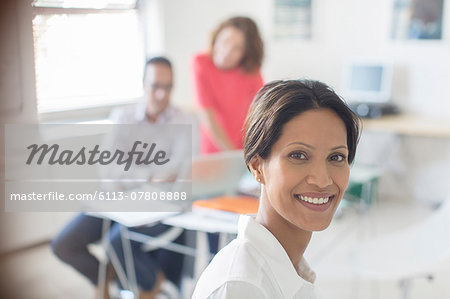 Portrait of smiling businesswoman in office, colleagues working in background