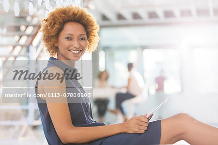 Portrait of smiling woman using digital tablet in office corridor, colleagues in background