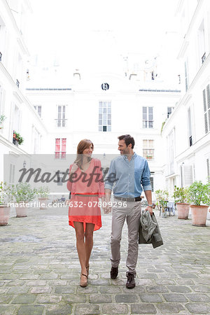 Couple holding hands walking together in building courtyard