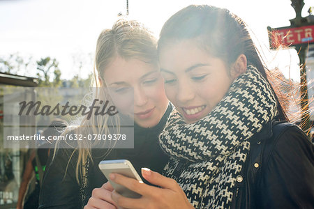 Young women outdoors looking at cell phone together