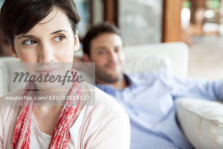 Woman looking away dreamily, man relaxing in background