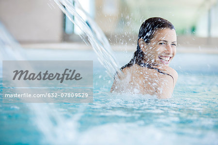 Woman relaxing under fountain in swimming pool